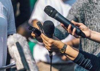 Journalists holding microphone and dictaphone, interviewing female speaker.